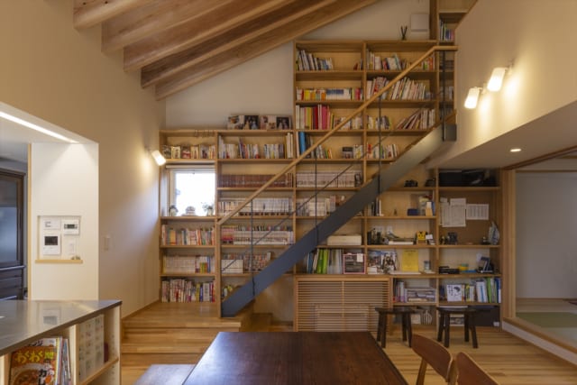 1階LDK。テラス側から階段を見る。「大きな本棚」との要望に応え、リビング内階段に沿って大容量の本棚を設置。生活動線上で蔵書が自然に目に入り、本が身近な存在になる。インテリアとしても魅力的で、ブックカフェのよう。階段下のルーバー部分の中には床下エアコンがある