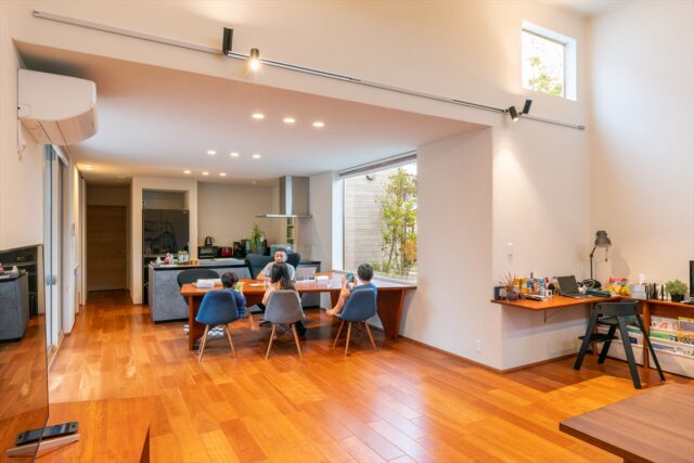 家族でダイニングテーブルを使用しているシーン。リビングの天井は高くされているため、広さだけでなく空間の広がりを感じることができる。リビングの角にはテーブルが造作されており、子どもたちが色々な場所で過ごすことができるように計算されている