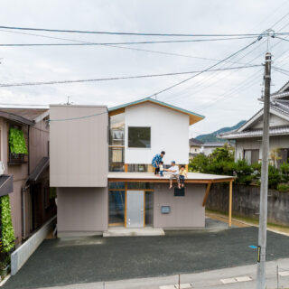 大きく張り出した庇は、きれいに手入れされた隣家の植栽とのつながりや平面的な広がりを考えて設置された。里道をはさんだ隣家の擁壁は2ｍの高さがあるため、まるで庇が隣家の地面につながっているように感じられる。同時に里道と敷地の、ゆるやかなつながりも実現している
