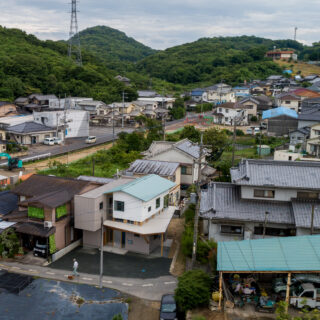 周辺環境。写真左側には比較的新しい家が並ぶ。家全体を2つにわけ、新しく建てられた周囲の家とボリュームが同じようになることを意識したのがよくわかる。切妻屋根は周囲に多く、色も周囲の家と近いものを使うなど、周囲に溶け込むプランとなっている
