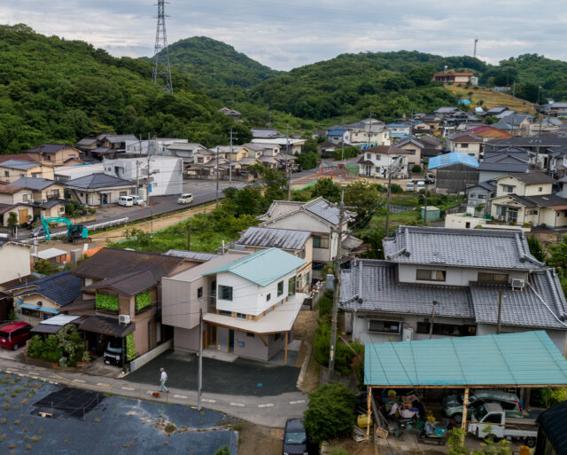 周辺環境。写真左側には比較的新しい家が並ぶ。家全体を2つにわけ、新しく建てられた周囲の家とボリュームが同じようになることを意識したのがよくわかる。切妻屋根は周囲に多く、色も周囲の家と近いものを使うなど、周囲に溶け込むプランとなっている
