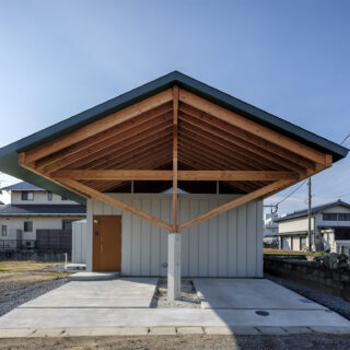 窓がない外観（正面）。切妻の大屋根が最大の特徴だ。柱を中央にすることで、雨で木の柱が傷まず、車の出し入れが容易になった。玄関ドアは外壁の縦のラインに合うように製作されている。木の梁に屋根が乗っているようなデザインにするため、軒の裏側も屋根と同じ色に塗装した
